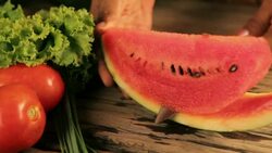Woman's hands cutting watermelon, behind fresh vegetables Stock Footage