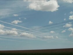 Driving by telephone poles and lines next to a corn field under white puffy clouds Stock Footage