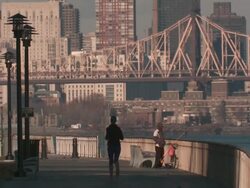 Woman jogging as a man is fishing while smoking a cigarette on a path along the east river in manhattan with the queensboro bridge in the background late in the day Stock Footage