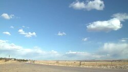 Semi truck carries a backhoe on a trailer and drives down a rural highway and passes a farm tractor discing a field. Stock Footage