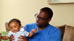 MS Father holding infant son on lap in living room while young daughter plays Stock Footage