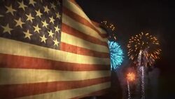 Fireworks explode behind an American flag waving in the wind. Stock Footage