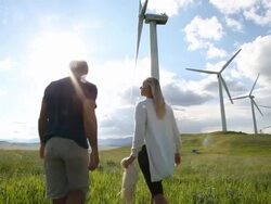 Wind turbines create electrical energy above couple in meadow, mountains Stock Footage