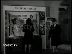 1946: THE CHILDREN'S BUREAU: EXT U.S. Children's Bureau building. INT lobby. INT Office w/ women working at table putting pamphlets together in mailing envelopes. Director of Children's Bureau Katherine F. Lenroot (1891-1982) at table, reading report. Instructional Video
