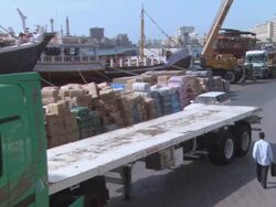 ZO Pedestrian walking away from a large construction site where a semi-truck backs up a little and stops as workers watch / Dubai, United Arab Emirates Stock Footage