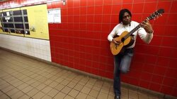 Man leans against wall playing acoustic guitar for tips in New York City subway Stock Footage