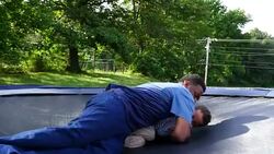 MS ZI Smiling father and young son wrestling on trampoline in backyard Stock Footage