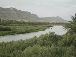 A river carves it's way through Moroccan vegetation and land, with mountains on the horizon. Stock Footage