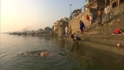 An old man dips his head in a sea near other bathers at a ghat in India. Stock Footage