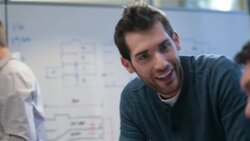 Trendy young businessman leads meeting in office conference-room; older businessman types on smart-phone Stock Footage