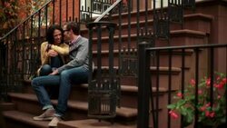 Hip young man kisses girlfriend on stoop of brownstone apartment (dolly-shot) Stock Footage