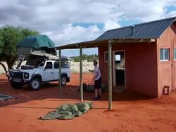 MS T/L Shot of Setting up camp with ATV beside ablution hut on intensely red earth surrounding by pale savannah and blue sky with scudding white clouds / Kalahari, Windhoek, Namibia Stock Footage