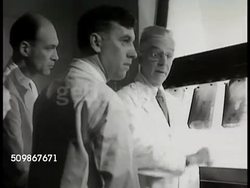 1948: HOSPITAL TESTING: X-Ray conference room sign over door. Surgeon, resident surgeon & family physician examining X-Rays on lightbox. X-ray showing gallbladder & stones. Doctors talking together, conference. Instructional Video