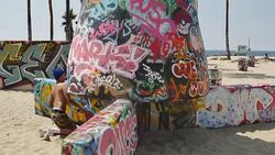 A graffiti artist spray paints at the Public Art Walls on the beach at the Pacific Ocean in Venice, California Stock Footage