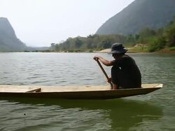 MS SLO MO Shot of Travelling following man rowing wooden canoe in river / Ou river, Luang Prabang, Laos Stock Footage