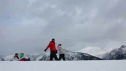 Family sledding on snowy hill below mountains Stock Footage