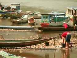 MS Shot of several small wooden boats mooring and girl washing clothes near river / Mountain village near Muang Ngoi, Luang Prabang, Laos Stock Footage