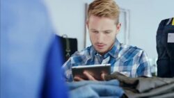 Young employee with tablet counts pants on shelf in modern clothing store Stock Footage