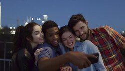 Group of friends pose for selfies and laugh together on scenic bridge at night Stock Footage
