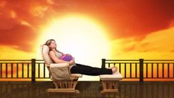 A pregnant woman relaxes in a glider against a computer generated blazing sunset Stock Footage