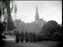 1944: IRELAND: ST PATRICK'S COLLEGE: WS Priests walking up road toward Pontifical University of Maynooth building. WS Priests walking on garden road walkway w/ college building BG. MS Male working at desk in front of garden window. Instructional Video