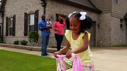 MS TS Smiling mother and father watching young daughter ride scooter in driveway of home Stock Footage