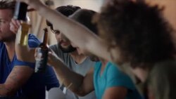 Guys sitting on couch watching tv and clinking bottles Stock Footage