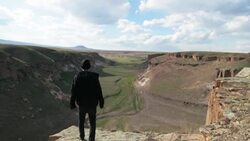 Man walking towards ledge, looking over riverbed in a valley in Ani, Eastern Anatolian. Stock Footage