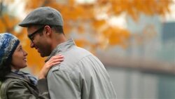 Young woman kisses boyfriend's forehead as he pulls her in close in autumn park Stock Footage