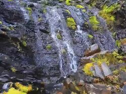 Water flowing over rock wall creating a small waterfalls Stock Footage
