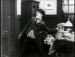 B/W 1916 man (Charlie Chaplin) throwing pie / it hits big man (Eric Campbell) / (2 shots) / short Stock Footage