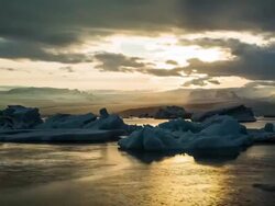 Timelapse of glacier ice beached in Jokulsarlon on black sand with clouds moving around. Camera dollies to the left and pans down. Stock Footage