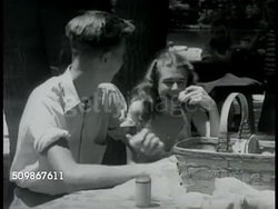 1945: TEENAGERS DATING: DRAMATIZATION: Teen boy & girl sitting outdoors at picnic table w/ food basket, talking, laughing. Young adult male & female couples on beach, talking, laughing, socializing. Instructional Video