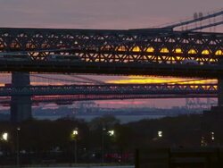 Time lapse shot of cars traveling over the Williamsburg Bridge in New York City. The sky is lit up with red , orange and purple colors. The Manhattan Bridge and Brooklyn Bridge can be seen in the distance Stock Footage