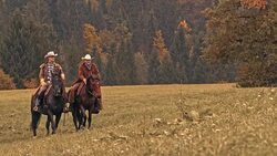 SLO MO Two smiling ranchers riding horses in mountain meadow Stock Footage