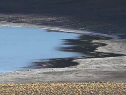 MS Multicolored landscape with blue water shimmering brown soil around it and yellow desert shrubs in ground Stock Footage