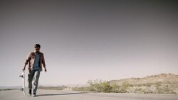 Young man walks up desert road carrying skateboard (slow-motion) Stock Footage