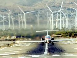 WS passenger jet takeoff fills air with hot fumes from jet engines against  background of spinning turbines of wind farm /Palm Springs, California, USA Stock Footage