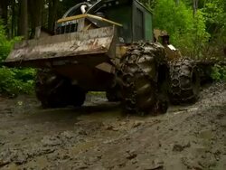 Full shot to close up of wheels of skidder as it drags trees through the mud, moving screen left toward the camera. Stock Footage