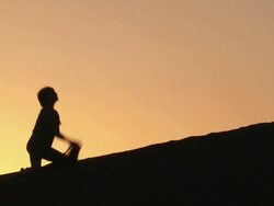 WS Children in silhouette against an orange sky on a sand dune playing, throwing, and digging in the sand / San Pedro de Atacama, Norte Grande, Chile Stock Footage