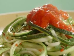 CU zucchini pasta on rotating dinner plate as marinara sauce is poured over the top and parmesan cheese sprinkled over the hot marinara Stock Footage
