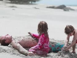 MS TD Boy and girl cover sand on man while boy throws sand on man and man gestures no on beach / Montezuma, Puntarenas, Costa Rica Stock Footage