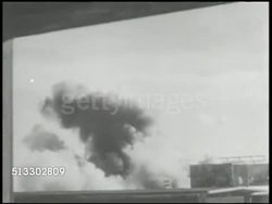 1942: BATTLE OF MIDWAY: VS Damaged & burning U.S. Midway Island air base, smoke, people running, flames & heavy smoke rising, light smoke passing Flag of America flying on pole. World War II, WWII, Pacific Front, airstrike, bombing, bombing run, raid Instructional Video