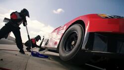 Stock car pit-crewman tightens tire lug-nuts, jackman lowers race-car Stock Footage
