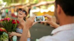 Cute Brazilian girl poses with colorful bouquets of flowers as boyfriend takes smartphone photos in Rio marketplace Stock Footage