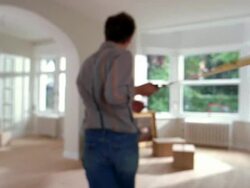 Medium shot man pulling tape measure across living room to arch w/boxes, chair and painting in background near windows Stock Footage