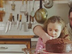 CU PAN Shot of Daddy and daughter sitting at kitchen table adding chocolate icing to cake / London, United Kingdom  Stock Footage