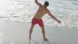 Young man doing cartwheels in surf at beach Stock Footage