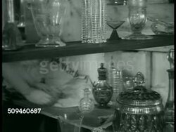 1938: CZECH EXPORT: MS Woman's hands, behind Czech-made Bohemian glassware displayed on shelves, wrapping glassware in paper. Man throwing ropes onto railroad car. HA WS Train moving (L) out of freight yard, moving on bridge.  Czechoslovakia. Instructional Video
