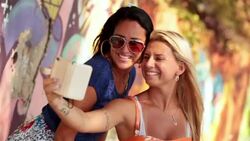 Two Brazilian girls take smartphone selfie by colorful wall graffiti in Rio Stock Footage